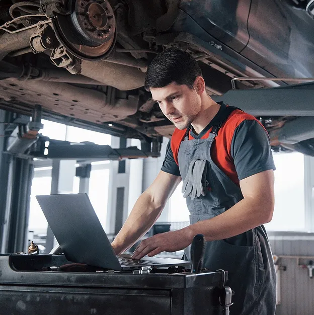 Mécanicien en salopette utilisant un ordinateur portable sous une voiture levée dans un garage à Auneau en Eure-et-Loir 28