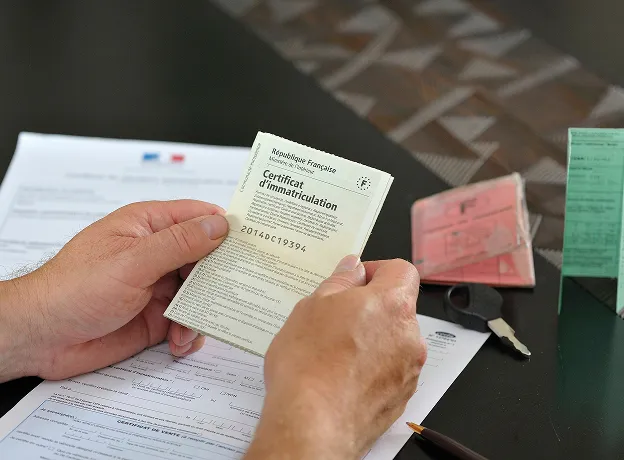 Mains tenant un certificat d'immatriculation français sur un bureau avec des documents à Auneau en Eure-et-Loir 28